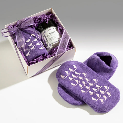 Purple slippers with decorative sole design.a jar of foot balm and a matching gift box on a light gray background