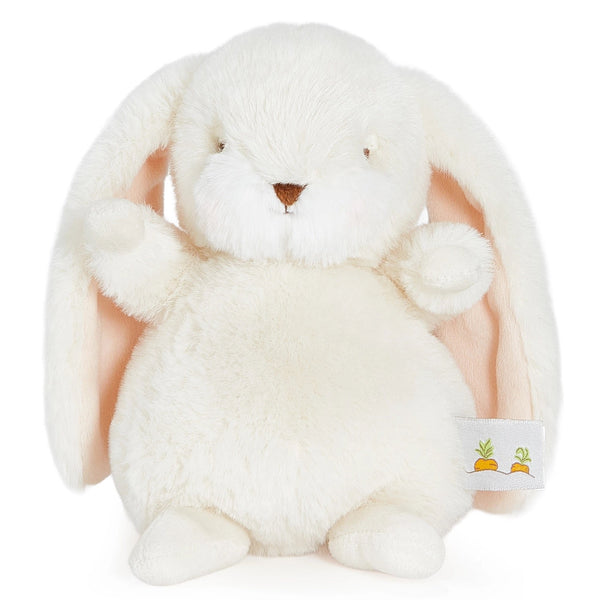 A plush bunny toy in creamy off-white faux fur with long floppy ears, a small brown embroidered nose, and a small fabric tag on the side, photographed on a clean white background.